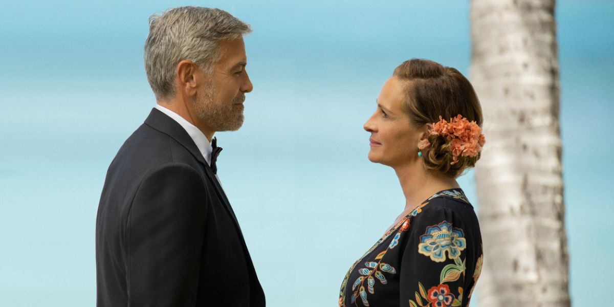 George Clooney in a tux and Julia Roberts in a floral dress with flowers in her hair, gazing into each other&rsquo;s eyes in Ticket To Paradise