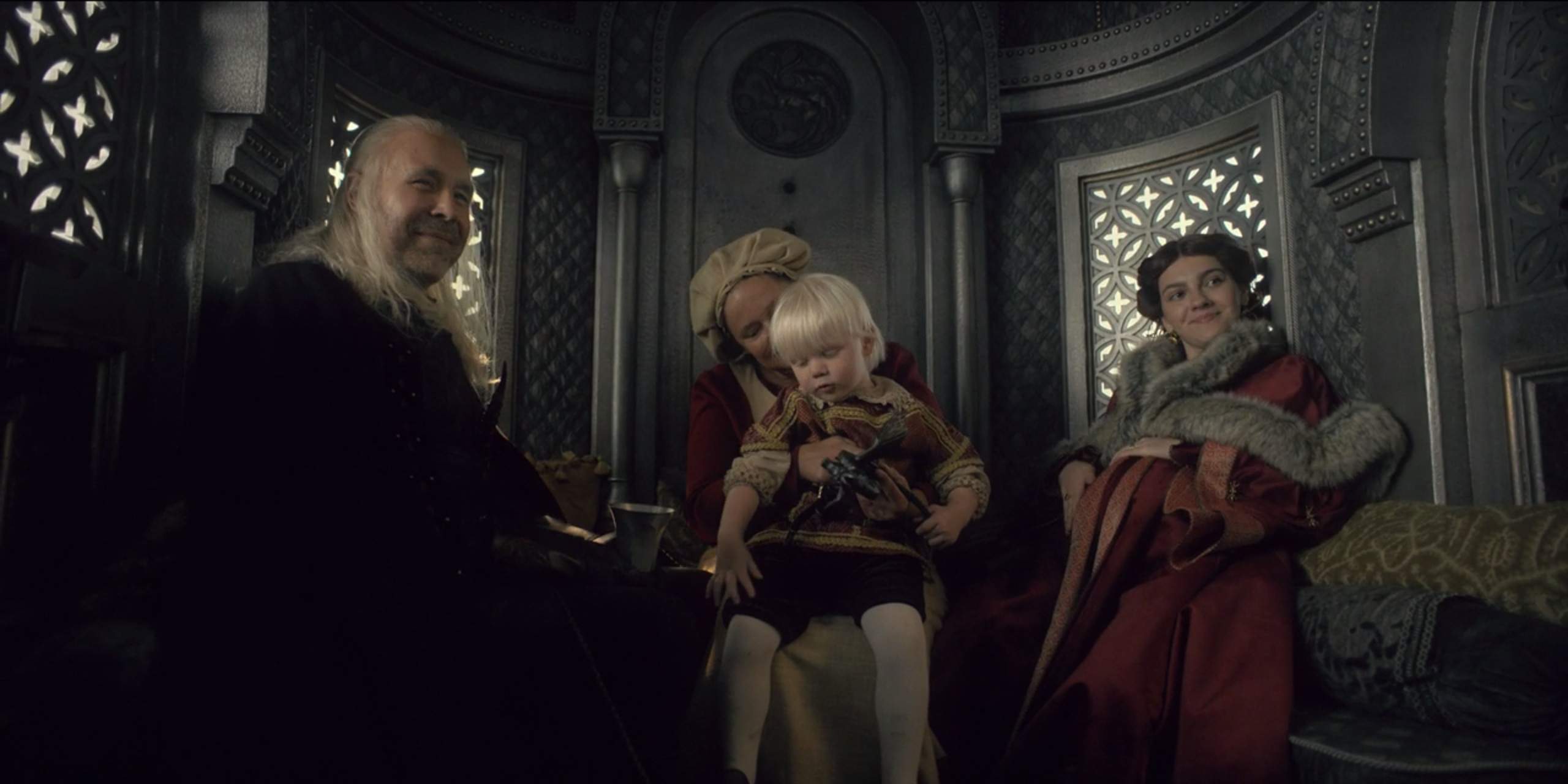 Viserys e Alicent sorrindo para Rhaenyra enquanto uma babá segura o Príncipe Aegon na Casa do Dragão