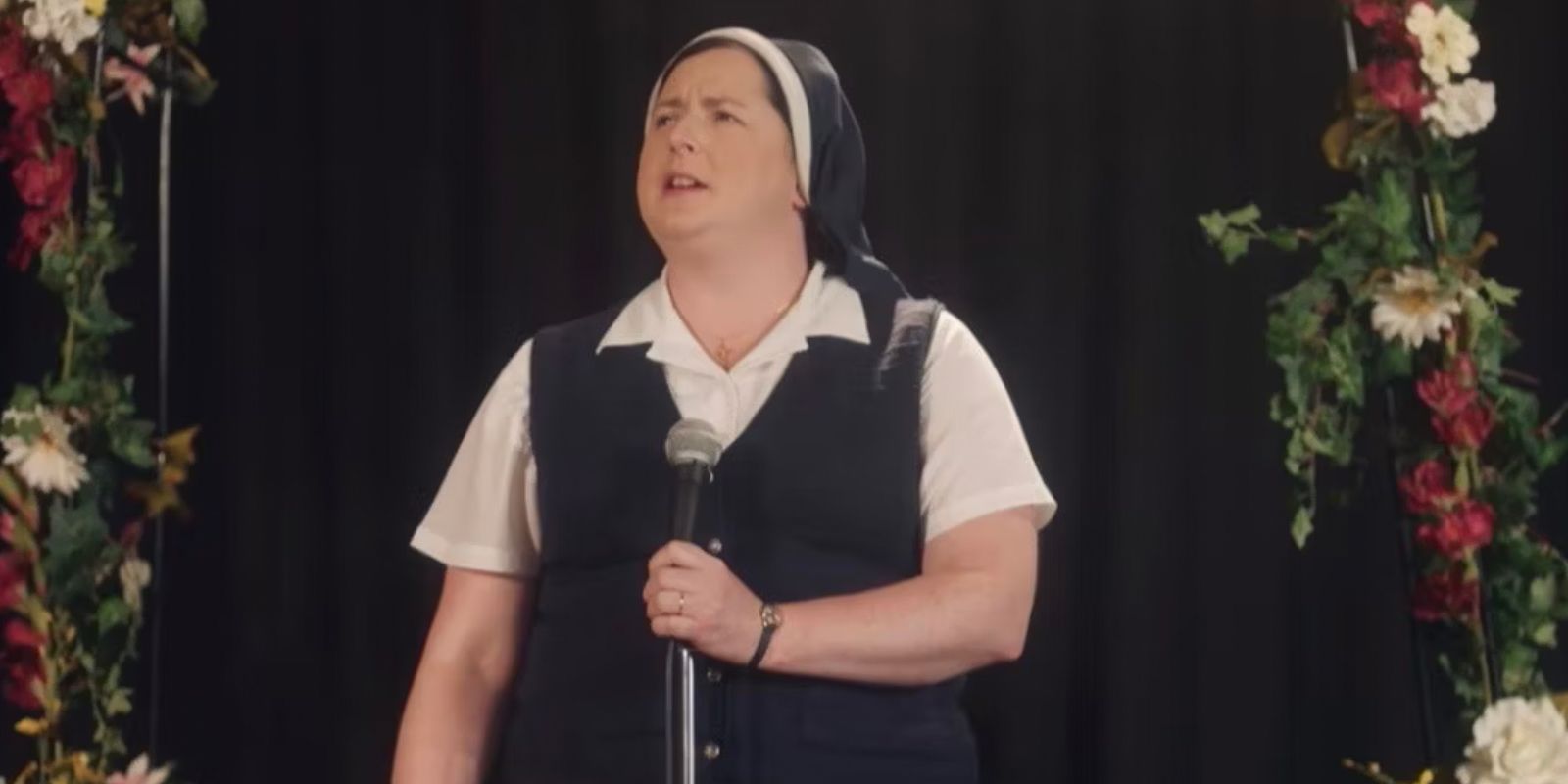 Sister Michael at the microphone on stage in Derry Girls