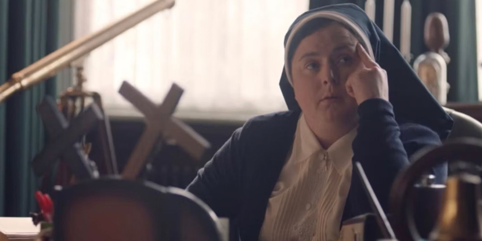 Sister Michael holds a finger to her head at her desk in Derry Girls