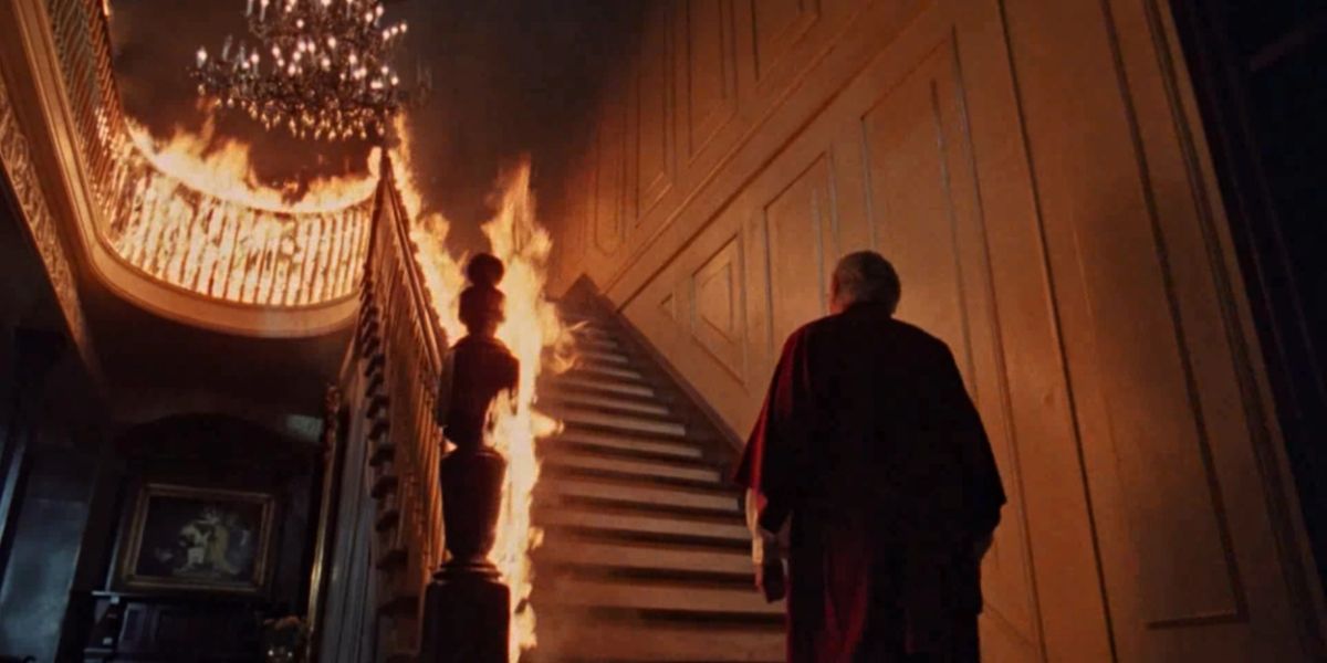 A staircase on fire with a man standing at the bottom, looking up in The Changeling