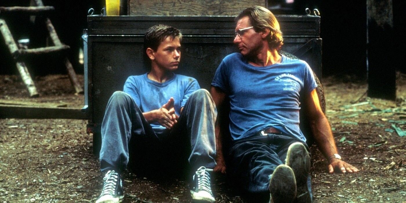 Harrison Ford and River Phoenix sitting on the ground in The Mosquito Coast