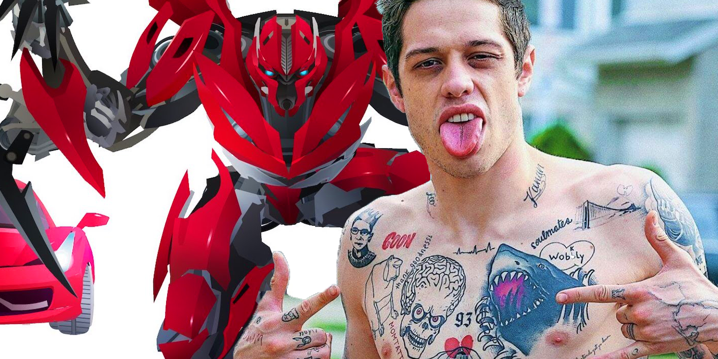 A man with tattoos stands in front of a red robot and makes a face