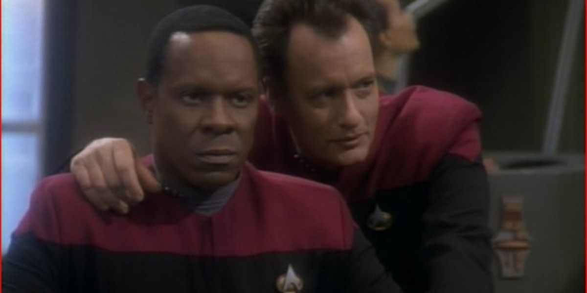 Uma foto do Capitão Sisko e Q é mostrada.