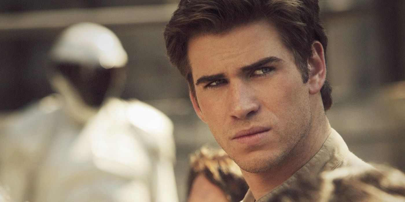 Gale Hawthorne (Liam Hemsworth) looking intense with Peacekeepers in the background in The Hunger Games.