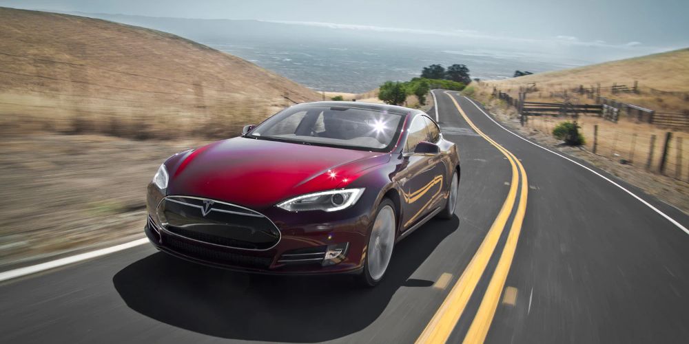 A red Tesla Model S drives by the ocean
