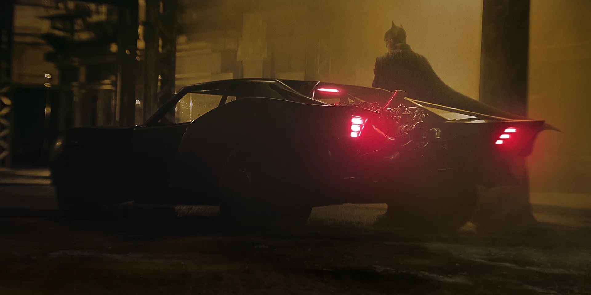 Batman standing next to the Batmobile in The Batman