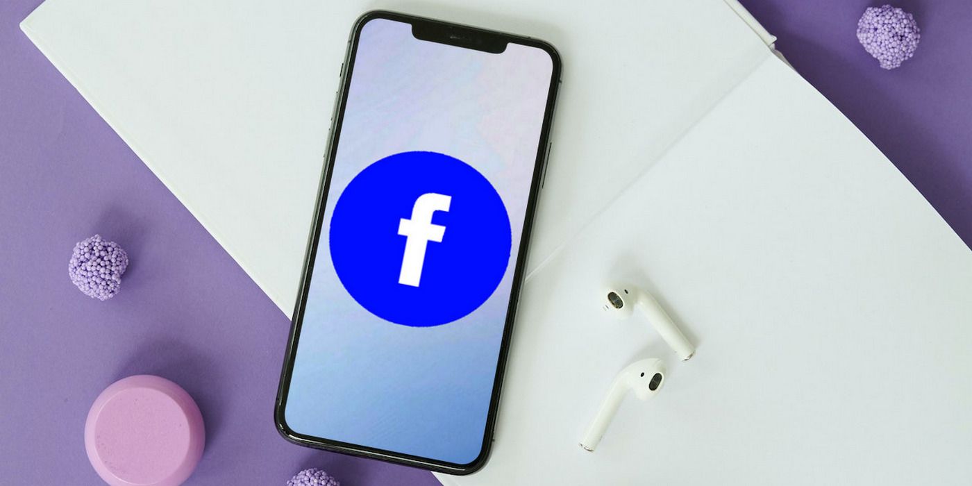 Facebook logo on iPhone 11, pictured on top of a blank sketchbook beside a pair of airpods