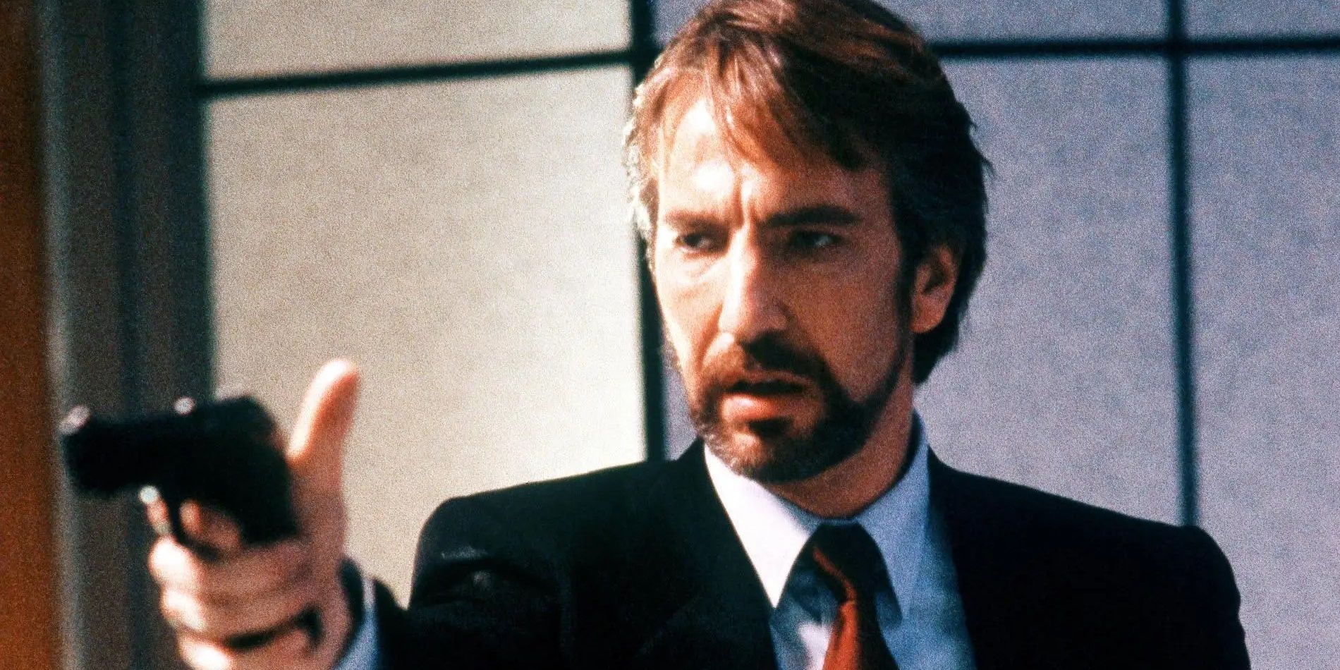 Alan Rickman as Hans Gruber pointing a gun in Die Hard