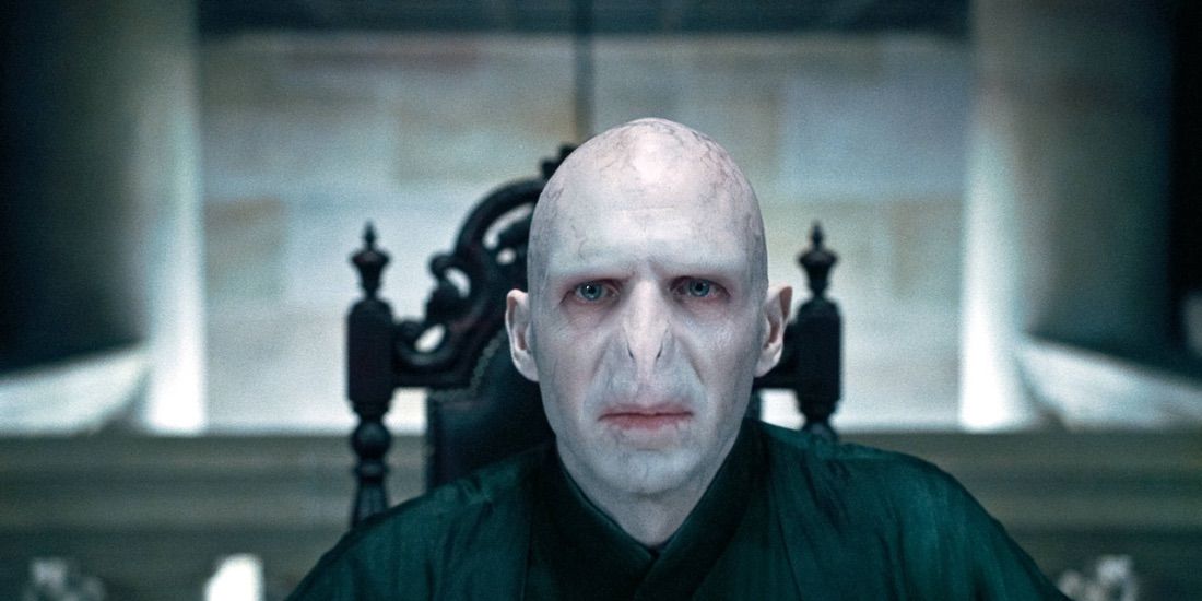 Lord Voldemort sentado à cabeceira de uma mesa em Harry Potter. 