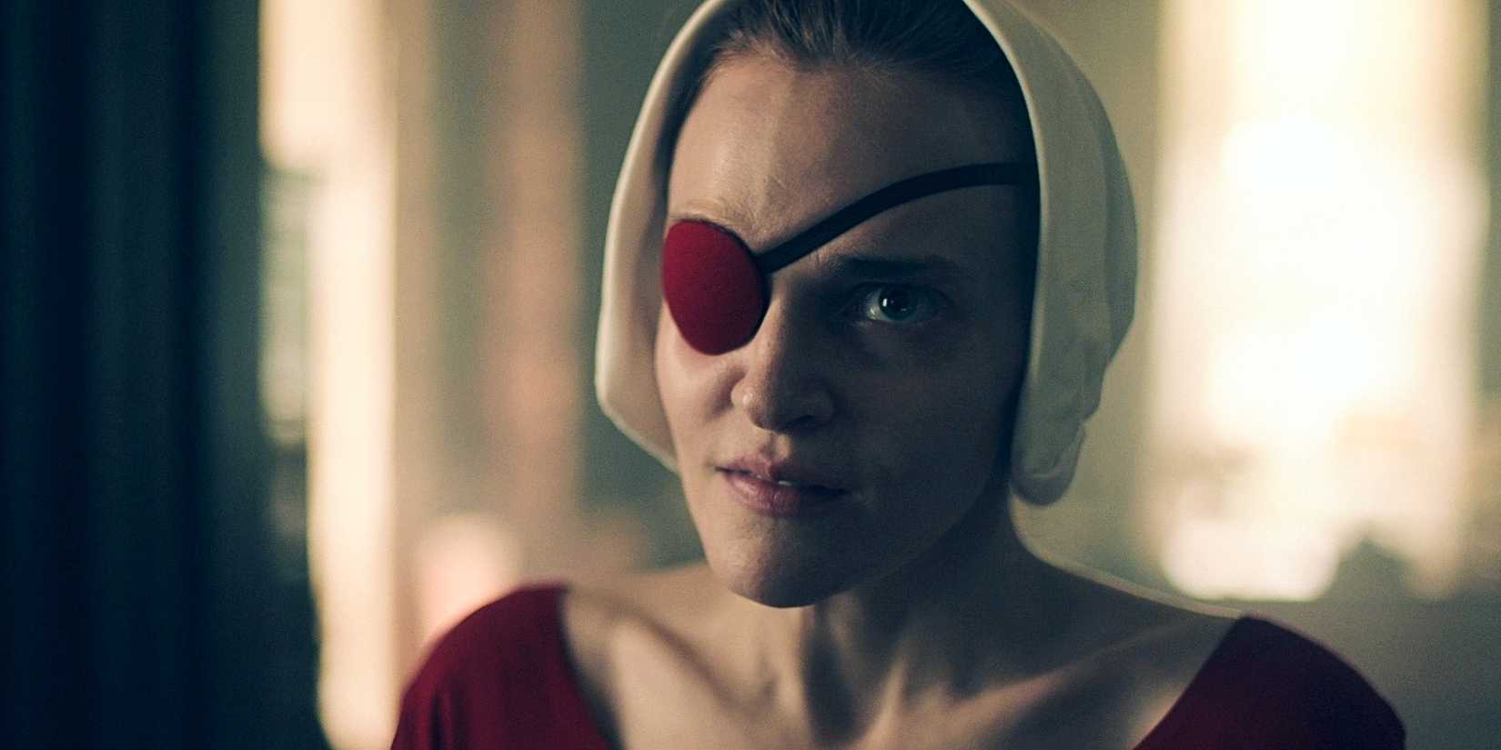 Janine (Madeline Brewer) with an eyepatch, smiling slightly in The Handmaid's Tale.