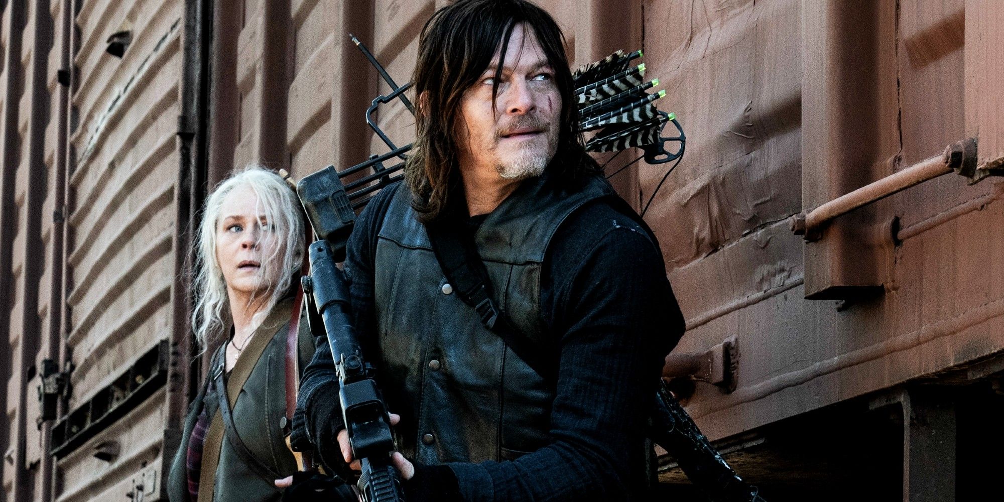 Melissa McBride as Carol and Norman Reedus as Daryl hiding behind a train car on The Walking Dead season 11