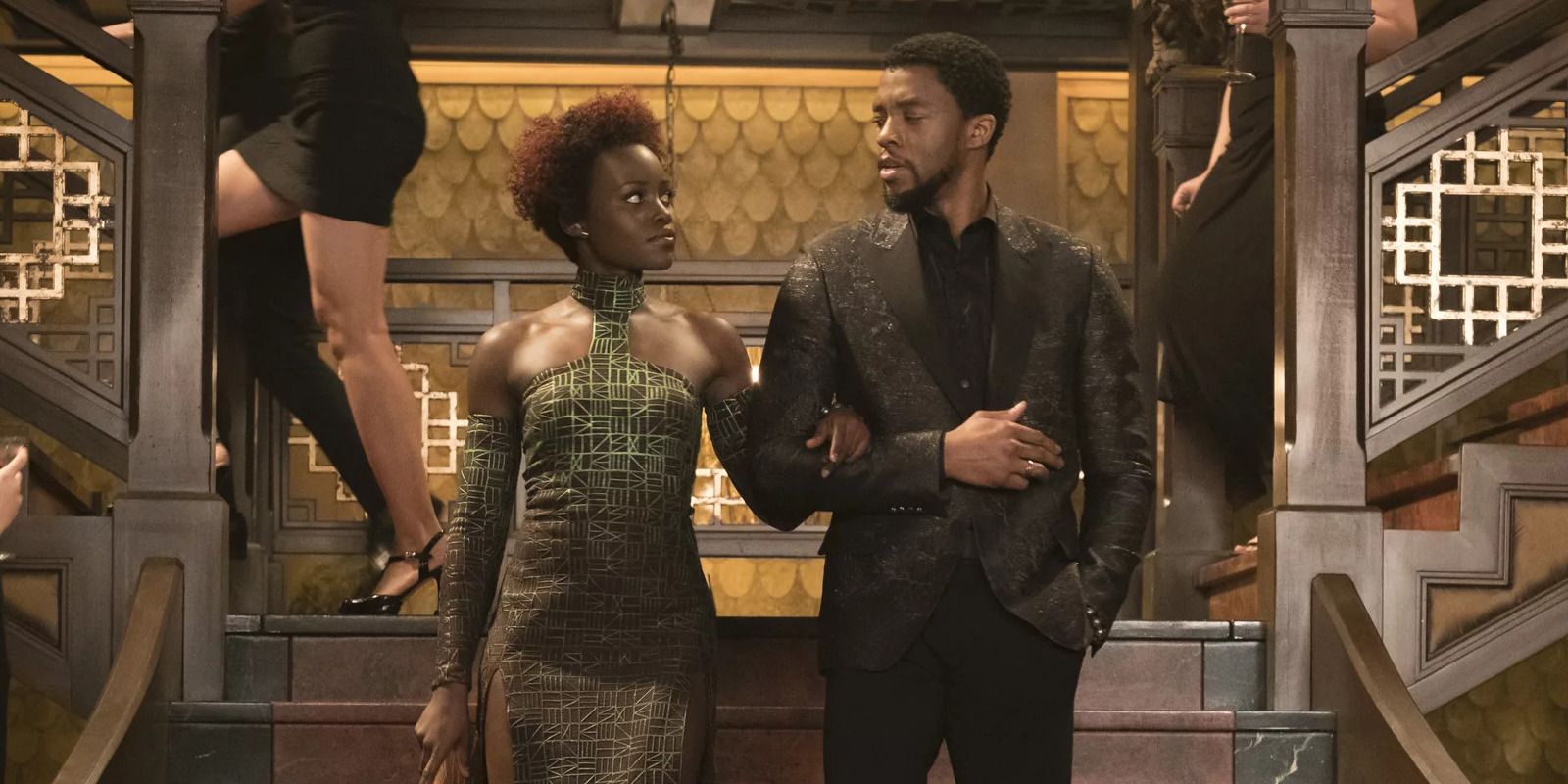 Nakia holds T'Challa's arm as they go down the stairs in Black Panther.