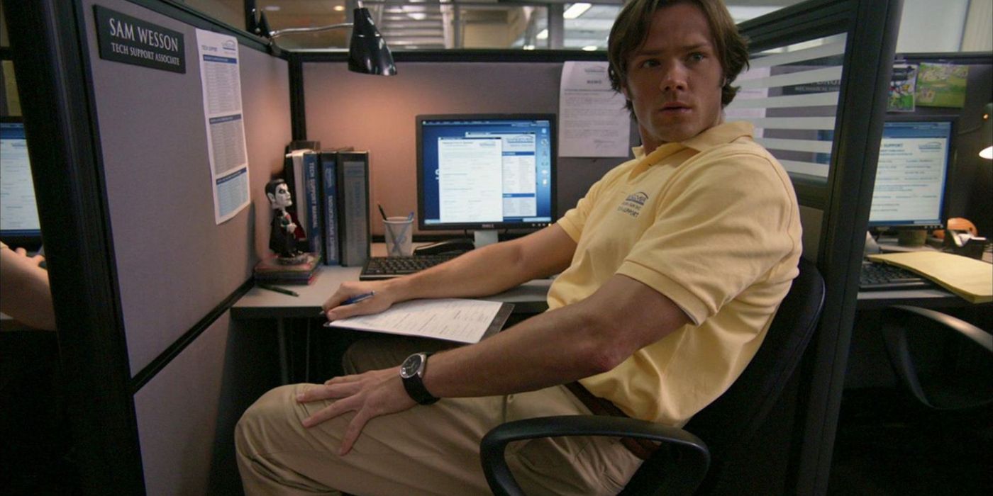 Sam Winchester sentado em um cubículo em Supernatural. 
