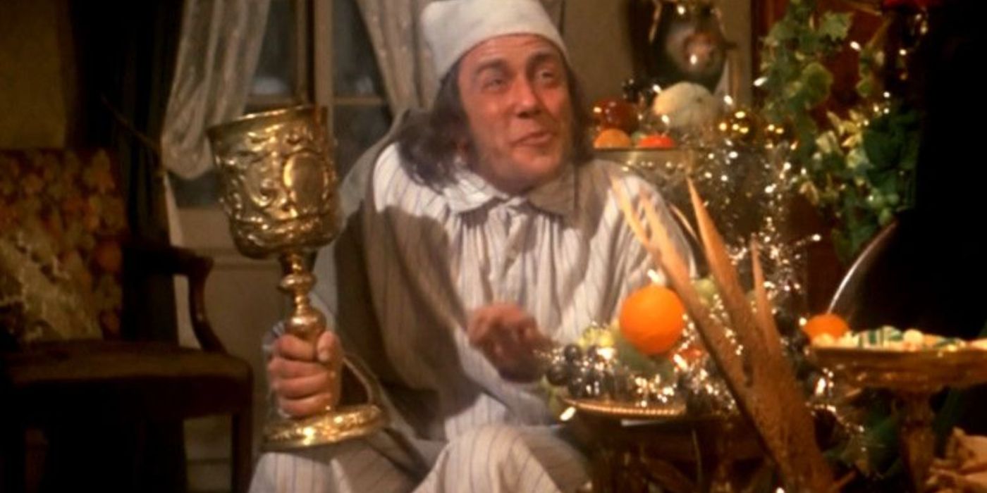 Scrooge duduk dan memegang piala emas raksasa di film Scrooge tahun 1970. 