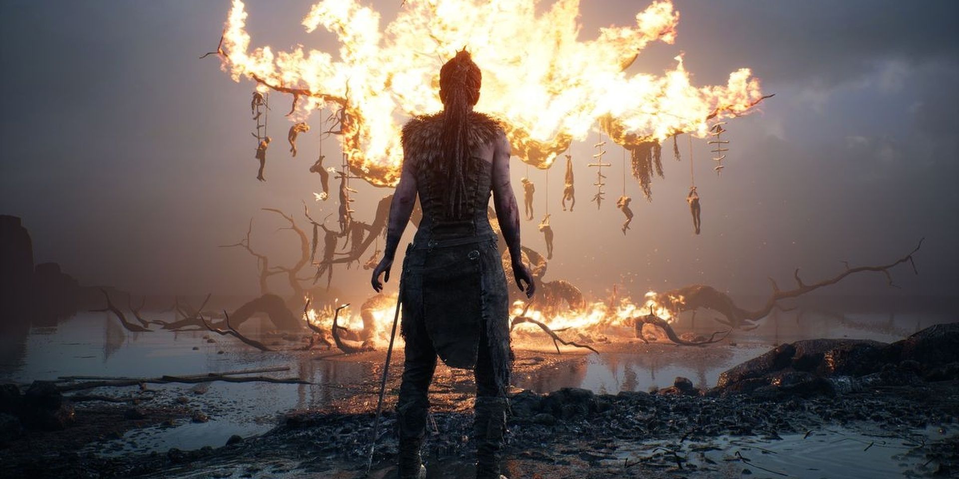 Senua from Hellblade - Senua's Sacrifice standing in front of a burning tree