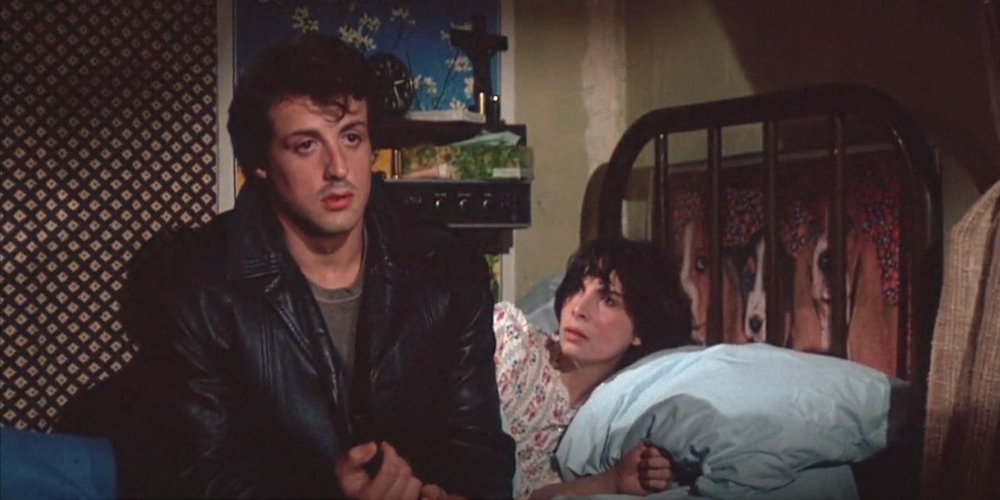 Sylvester Stallone como Rocky em uma jaqueta de couro sentado na cama confessando seus medos para Talia Shire como Adrian, que está deitado na cama olhando para Rocky com atenção