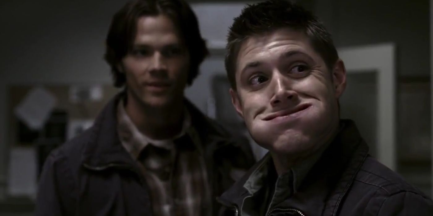 Dean com a boca cheia de comida com Sam ao fundo em Supernatural. 