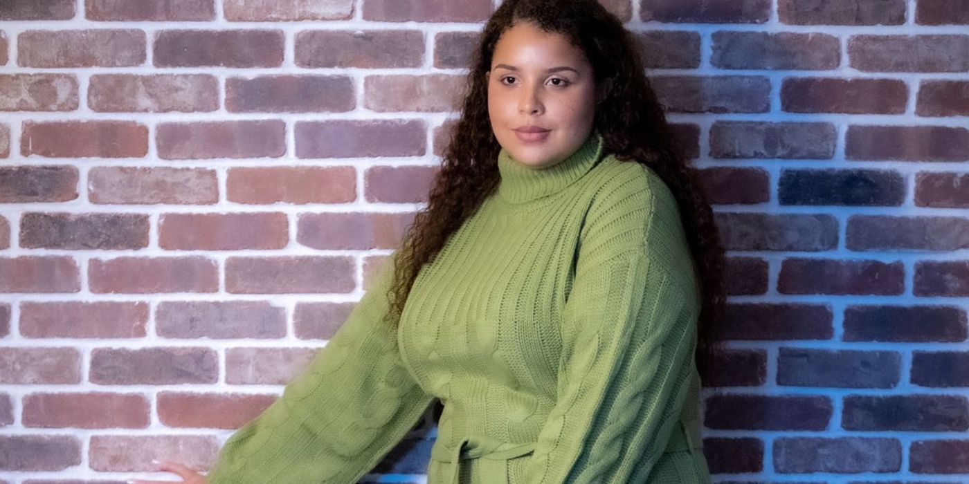 A estrela de Family Chantel, Winter Everett, usando um vestido de suéter verde e modelando contra a parede de tijolos