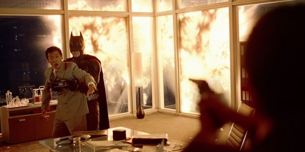Batman holds Lau hostage with an explosion behind them in The Dark Knight 