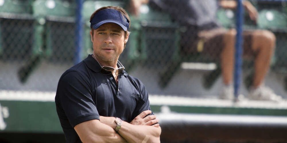 Brad Pitt em pé com os braços cruzados em Moneyball 