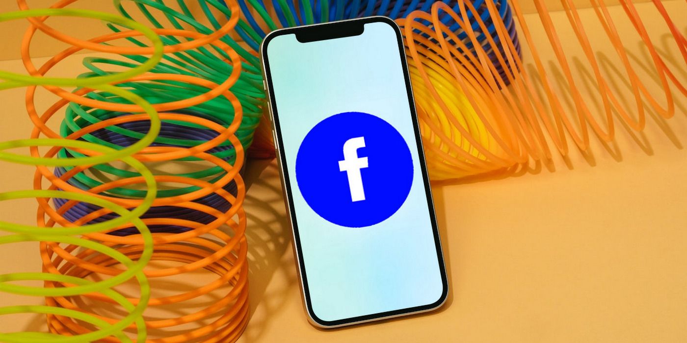 Facebook logo on iPhone 12 pictured on an orange background with orange and green springs around