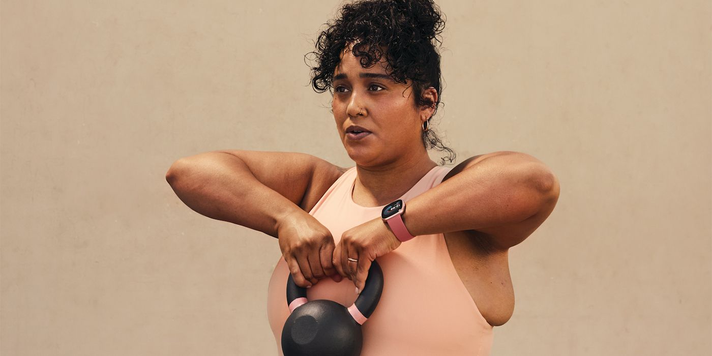 mulher levantando um kettlebell enquanto usava o fitbit versa 4