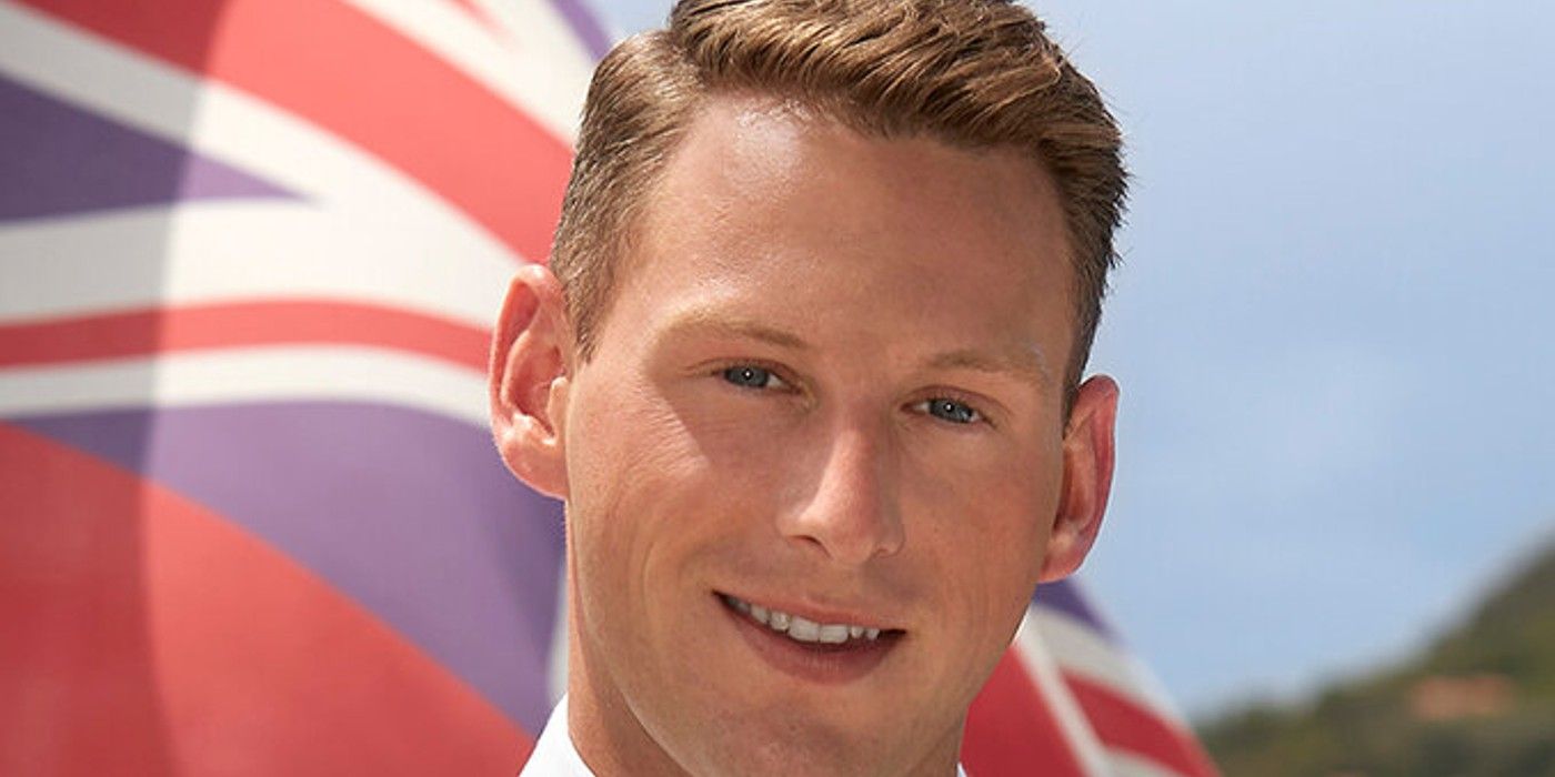 Fraser Olender From Below Deck smiling in front of a flag closeup