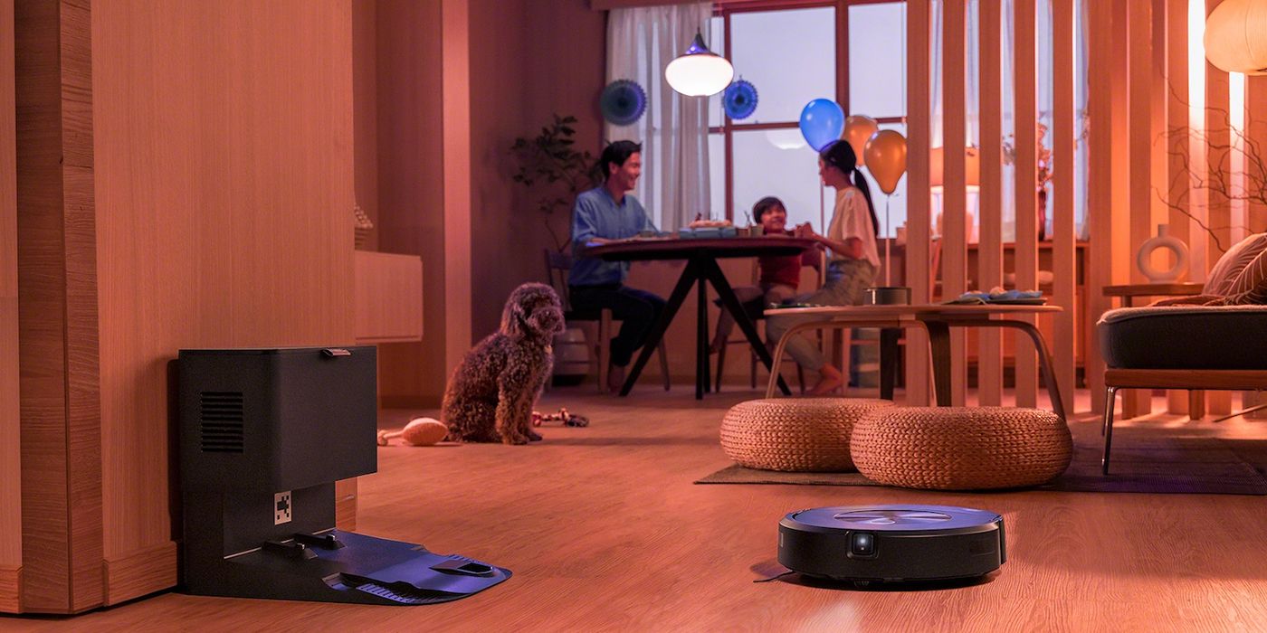 Lifestyle image of a family at the kitchen table in the background, the iRobot Roomba j7+ robot vacuum in the foreground.