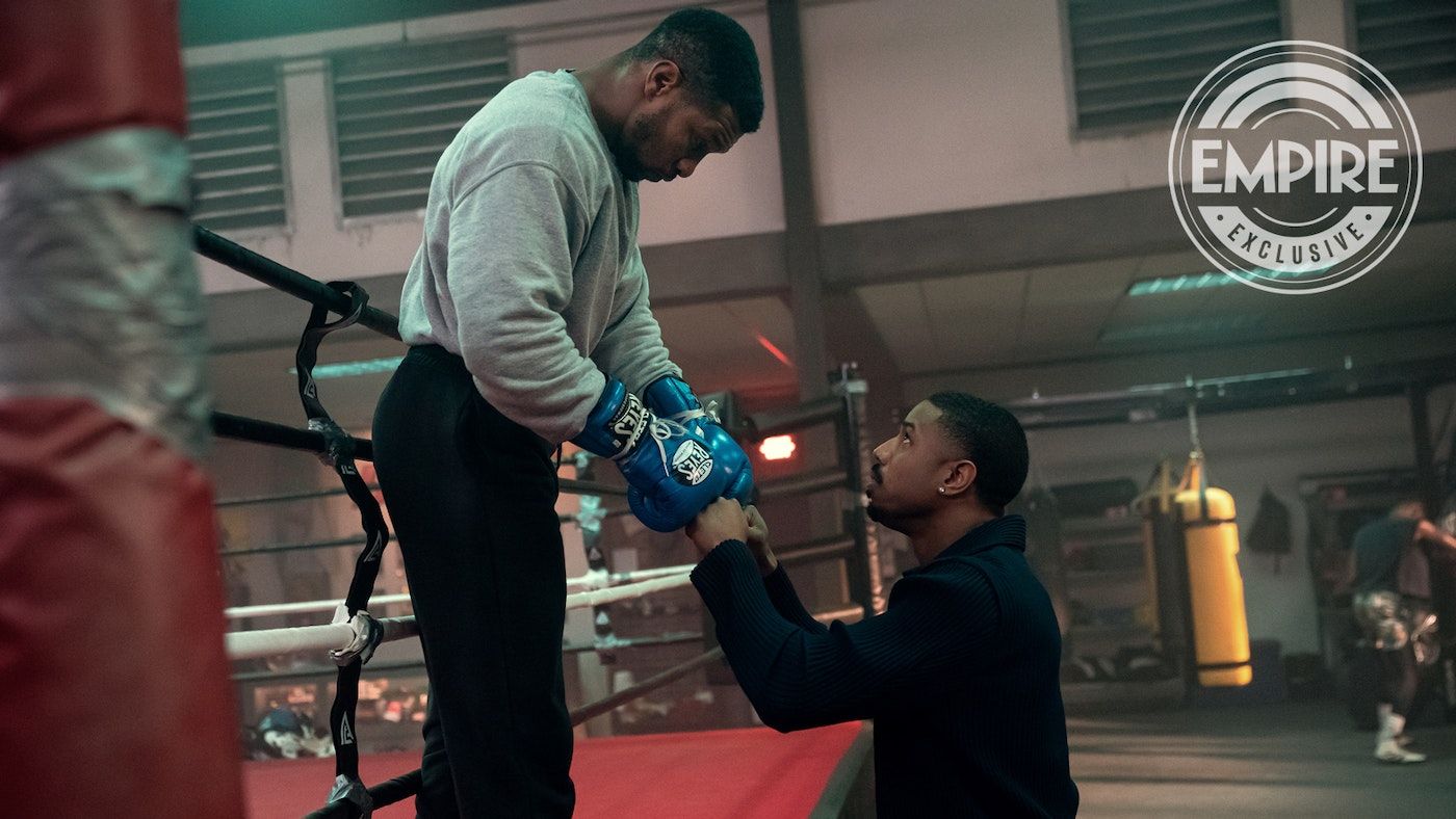 Jonathan Majors as Damian stands on the edge of a boxing ring bumping his gloves into the fists of Michael B Jordan as Adonis in Creed 3