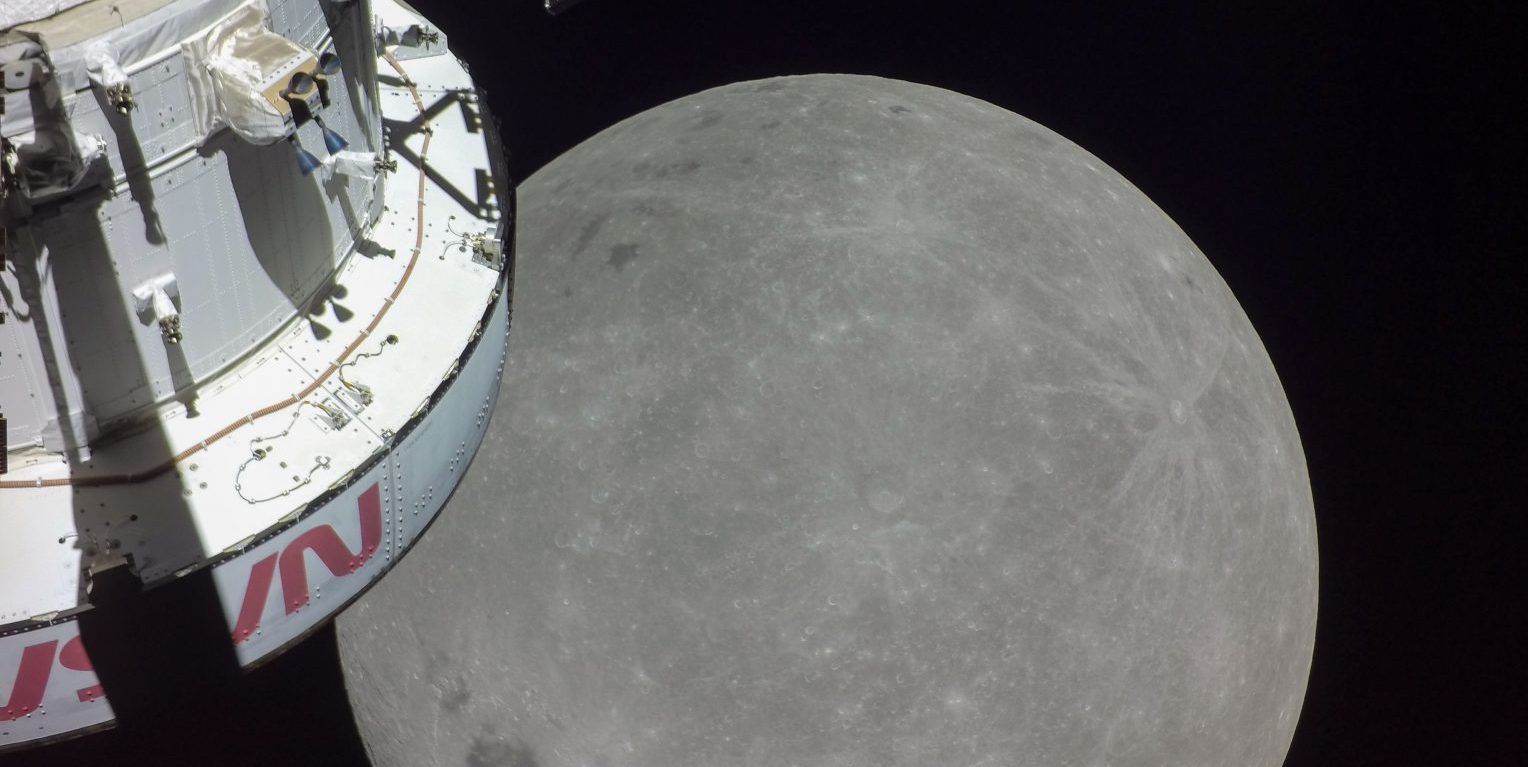 Parte da espaçonave Orion é retratada (à esquerda) em frente a uma grande visão da lua (centro inferior) durante seu sobrevoo próximo