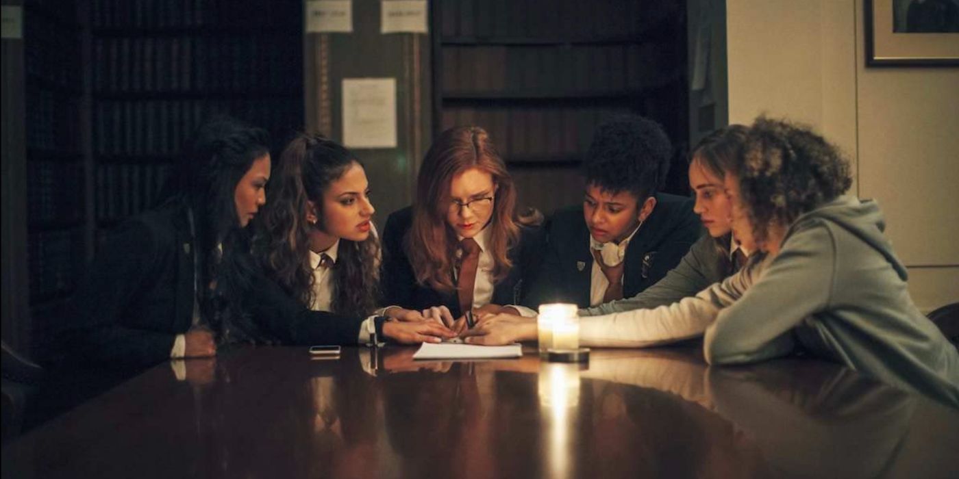 Um grupo de garotas reunidas em torno de uma mesa se tocando em Seance (2021). 