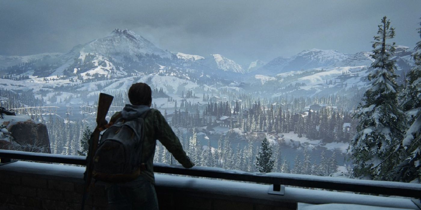 Character looking out over the winter landscape, with snow-tipped mountains and a frozen lake surrounded by trees in The Last of Us 2