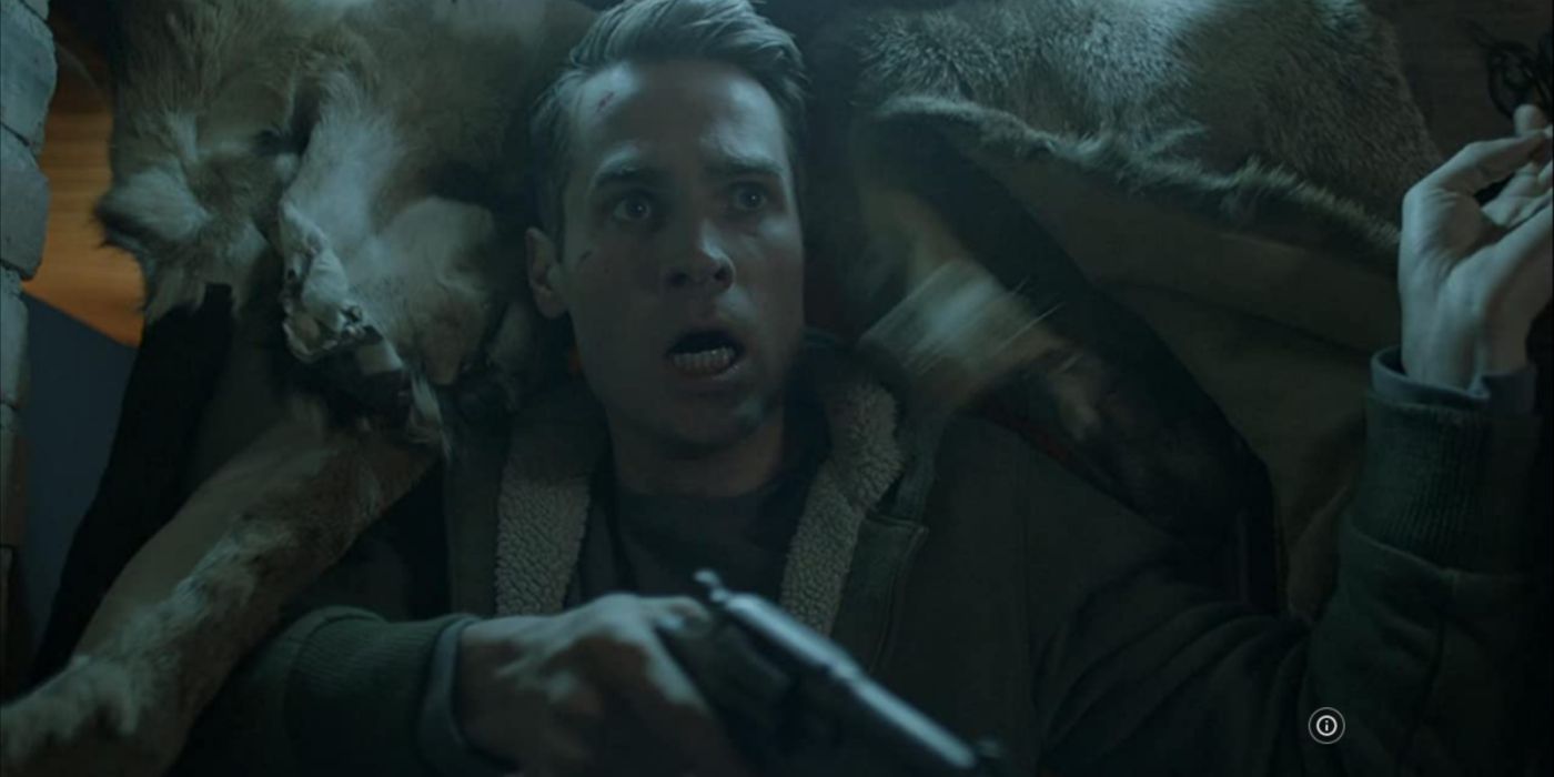 John olhando assustado contra uma pele de animal com uma arma na mão em O Lobo de Snow Hollow. 