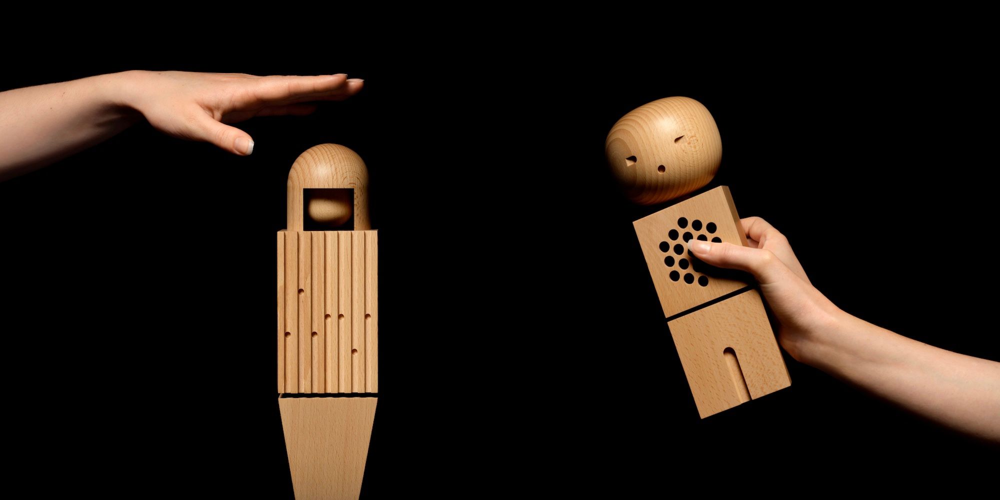 Duas das bonecas de madeira do coro da Teenage Engineering são retratadas contra um fundo preto.  À esquerda, uma mão fica acima da figura como se fosse bater em sua cabeça, enquanto a figura à direita é segurada na mão de uma pessoa inclinada para o lado