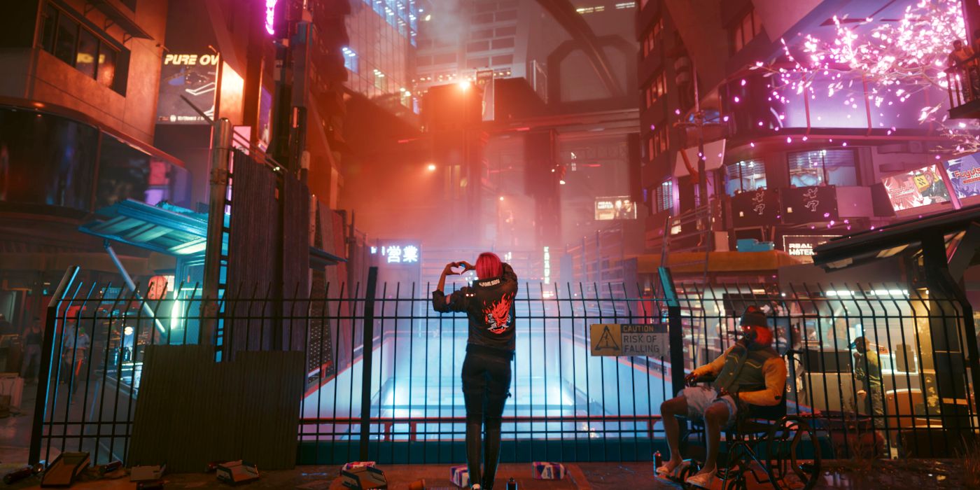 A player's character standing in front of a fence in Night City, making a heart with their hands in Cyberpunk 2077.
