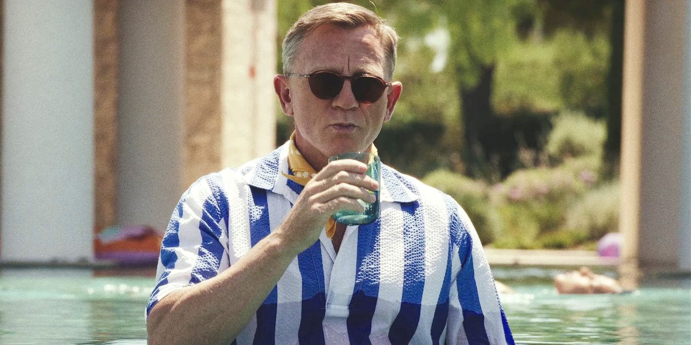 Daniel Craig as Benoit Blanc in Knives Out 2, drinking from a glass while standing fully dressed in a pool