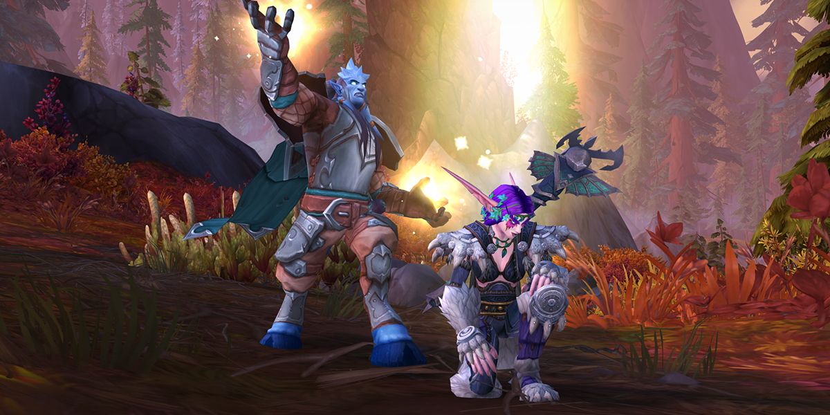 Twee World of Warcraft-personages in een bebost, bergachtig gebied - de een knielt met de ander erachter en spreekt een spreuk uit van gloeiende palmen.