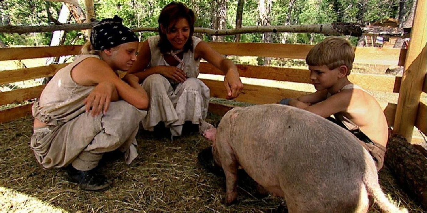 Frontier House: uma mulher e duas crianças alimentam um porco em um curral