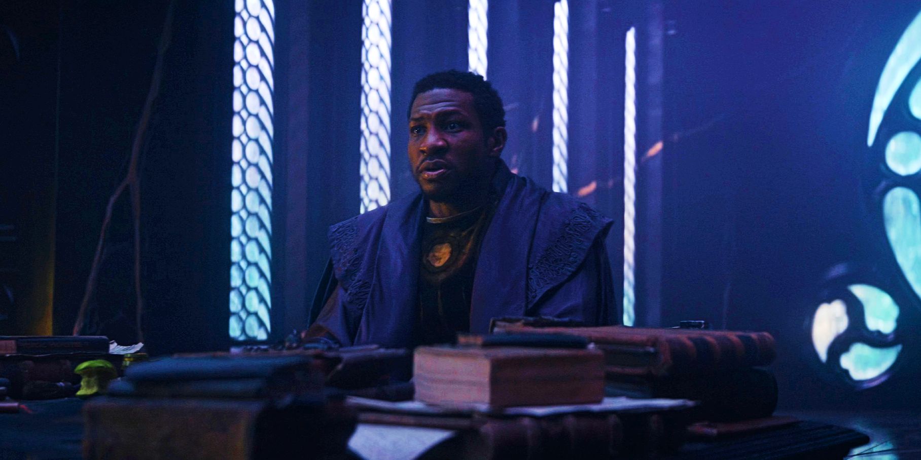 Jonathan Majors como Kang, o Conquistador, sentado atrás da mesa no final da primeira temporada de Loki