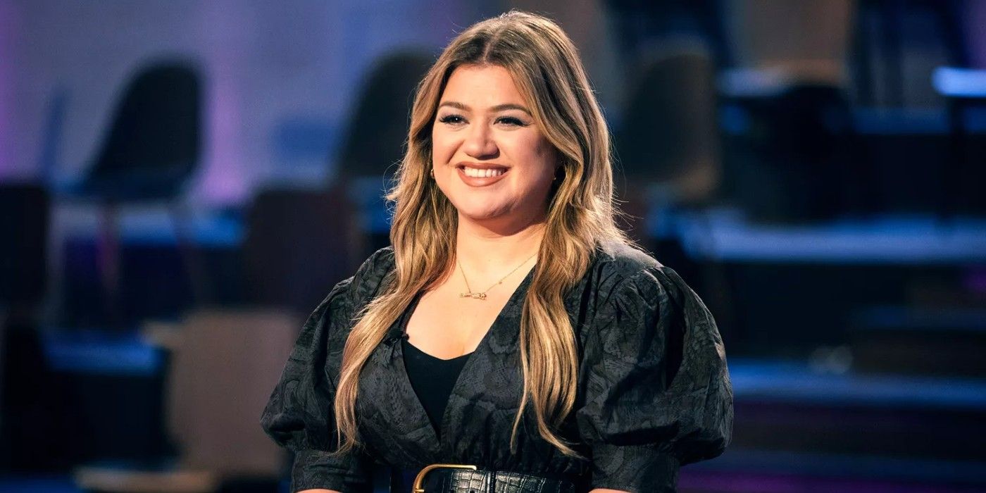 Kelly Clarkson The Voice smiling in dark outfit in studio 