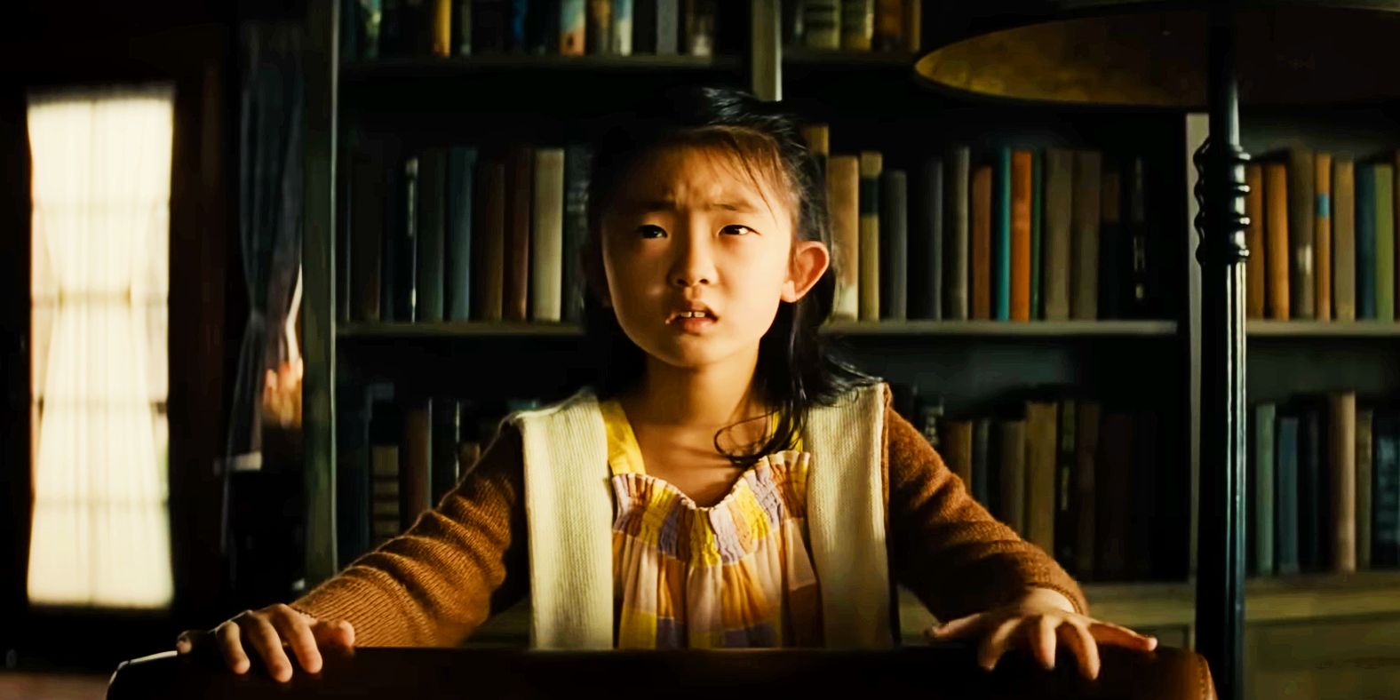 Kristen Cui as Wen looking scared in front of book shelf in Knock at the Cabin