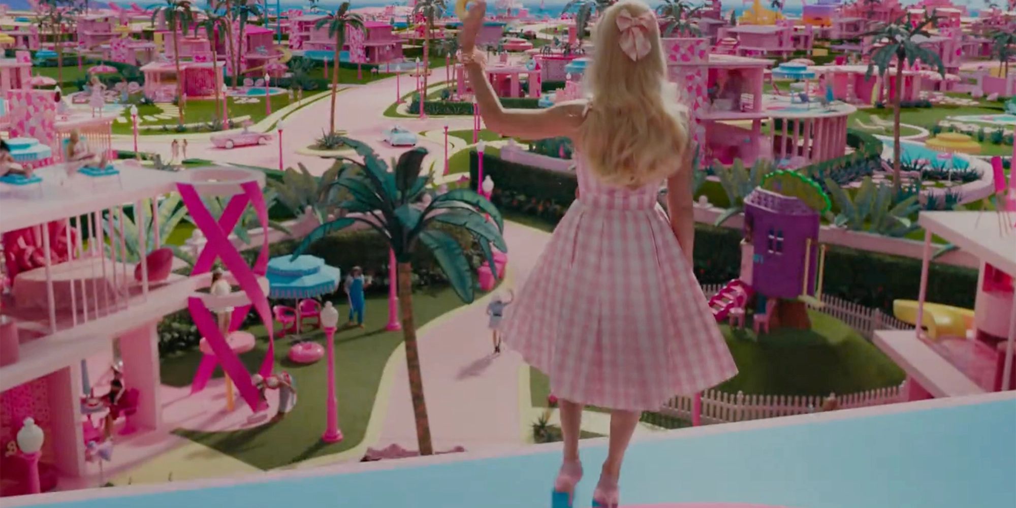 Margot Robbie waves at a pastel pink toy town in Barbie movie