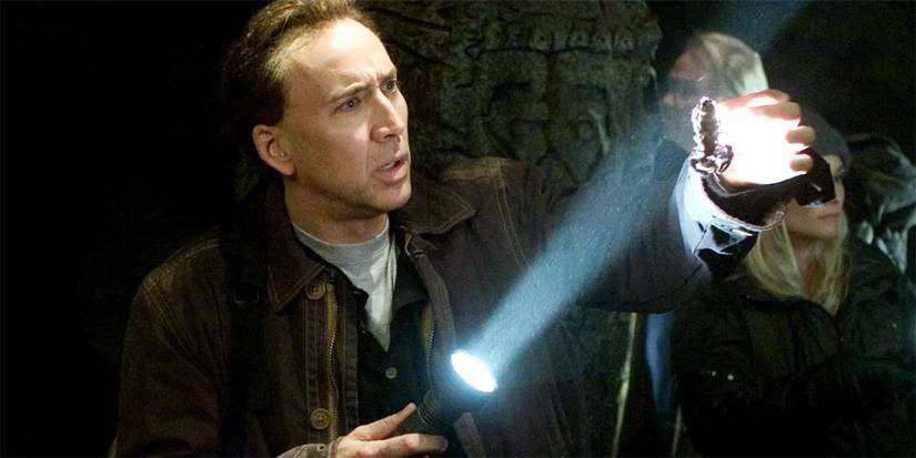 Nicolas Cage as Benjamin Gates pointing a flashlight at something in his hand in National Treasure