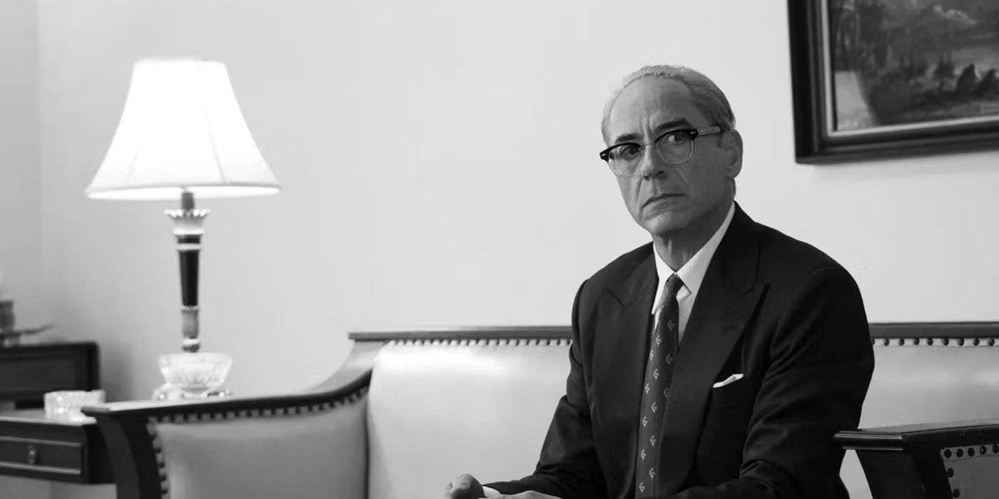 A black and white image of Robert Downey Jr as Lewis Strauss seated and looking serious in Oppenheimer