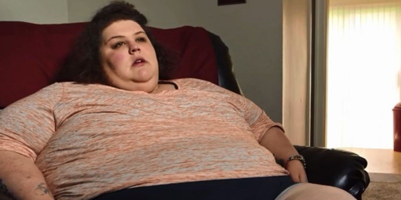 Sarah Neeley from My 600 Lb Life season 6 sitting on a black leather chair with a red blanket behind her 