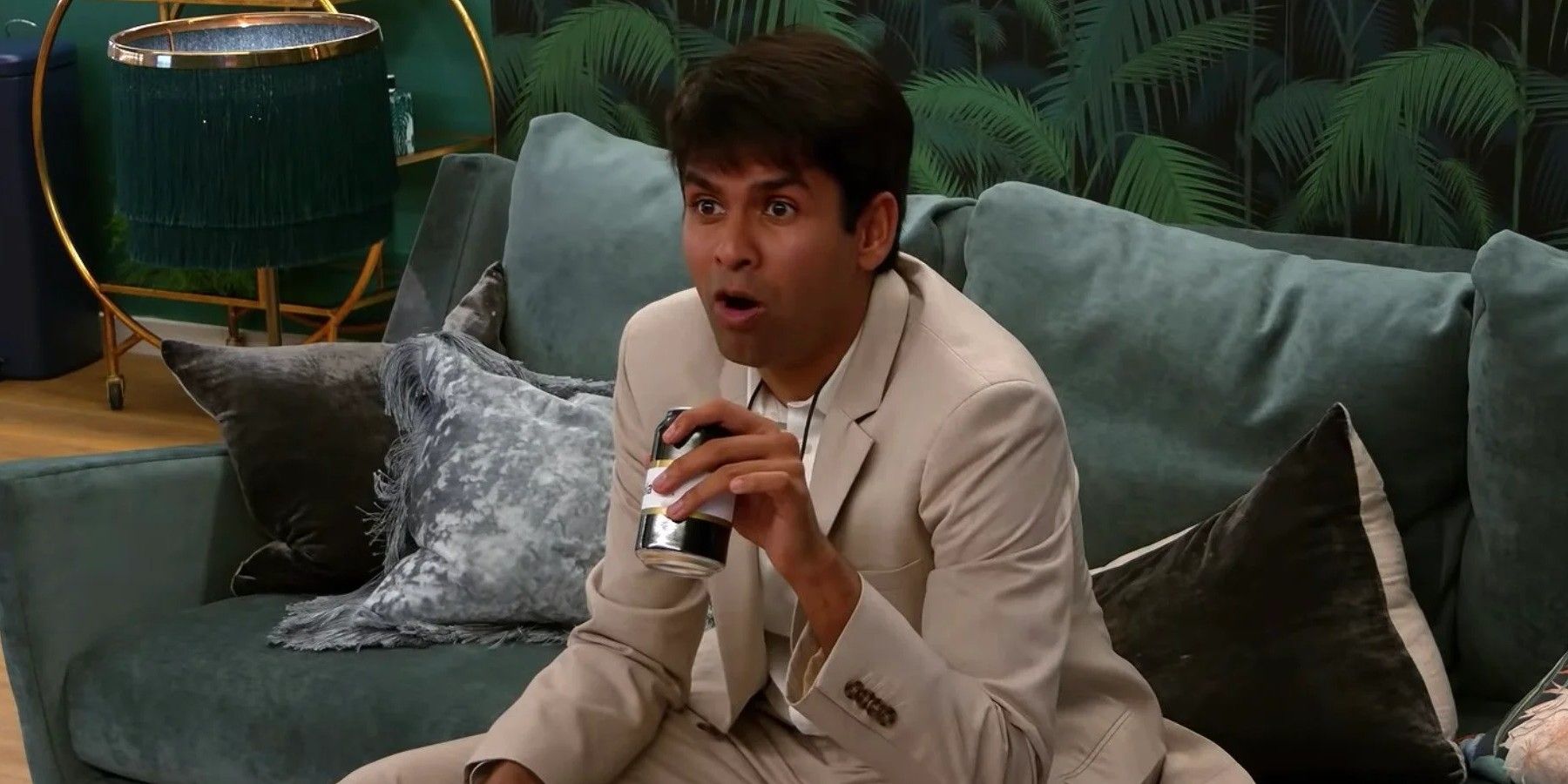 Shubham reacts in surprise while sitting on the couch holding a beverage can in his apartment on The Circle.