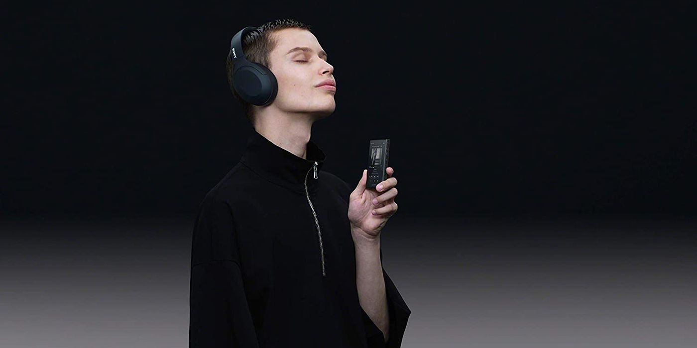 young man with a new Sony Walkman wearing headphones and holding it on a black background.