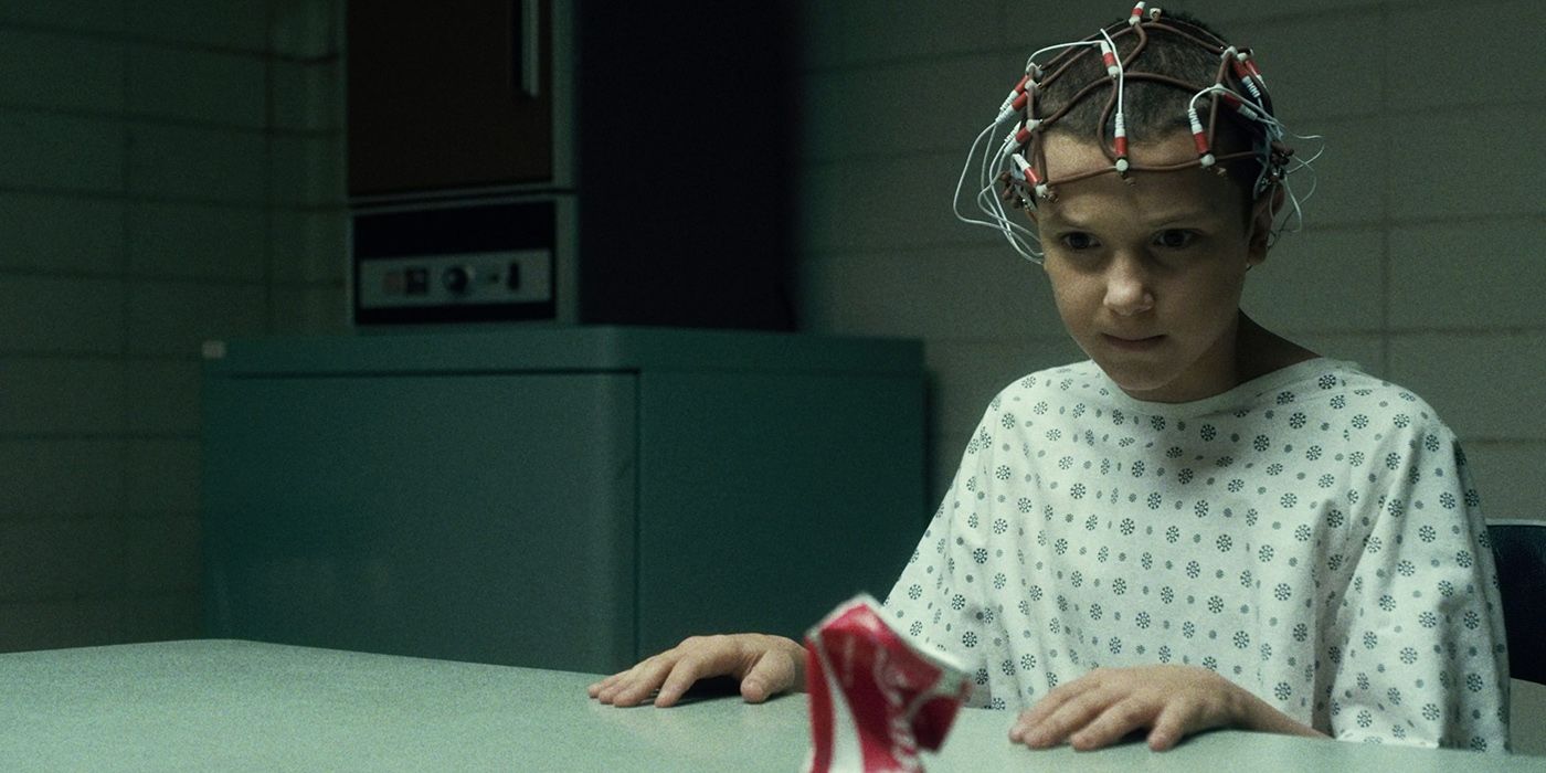 Eleven from Stranger Things at Hawkins Labs, sensors around her head with a bent Coca Cola can in front of her.