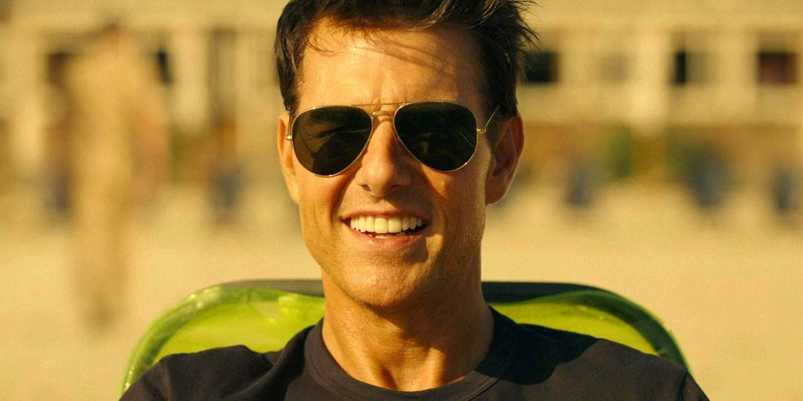 Tom Cruise as Maverick wearing sunglasses and smiling while seated in Top Gun Maverick